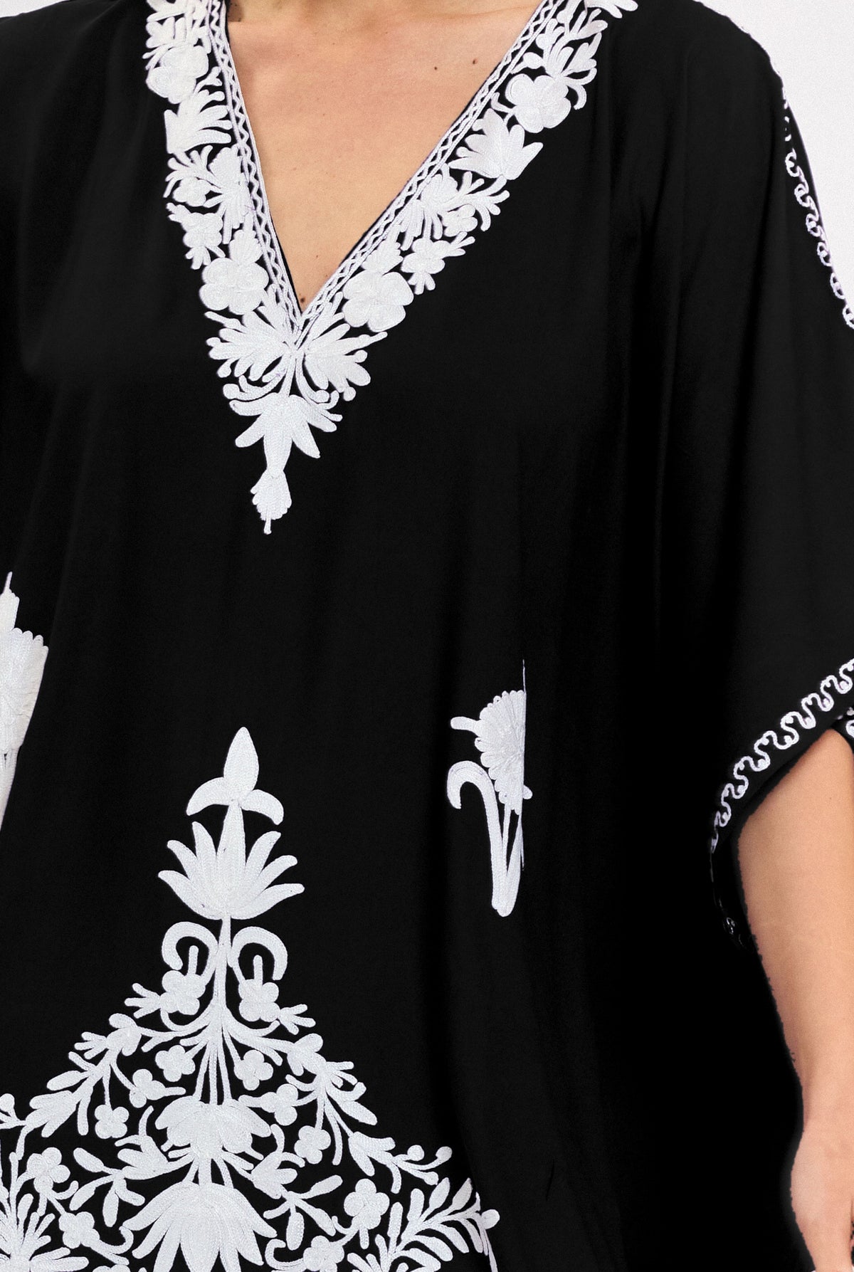 Close-up of the hand-embroidered V-neckline on the black Kashmir cotton kaftan, white threadwork